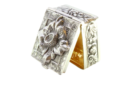 Caixa de comprimidos em prata com flor revelada na tampa e interior em dourado.